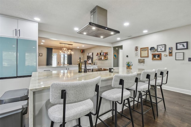 kitchen featuring a kitchen breakfast bar, light stone counters, island exhaust hood, pendant lighting, and white cabinets