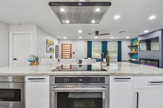 kitchen with oven, wall chimney exhaust hood, light stone countertops, black electric cooktop, and white cabinetry