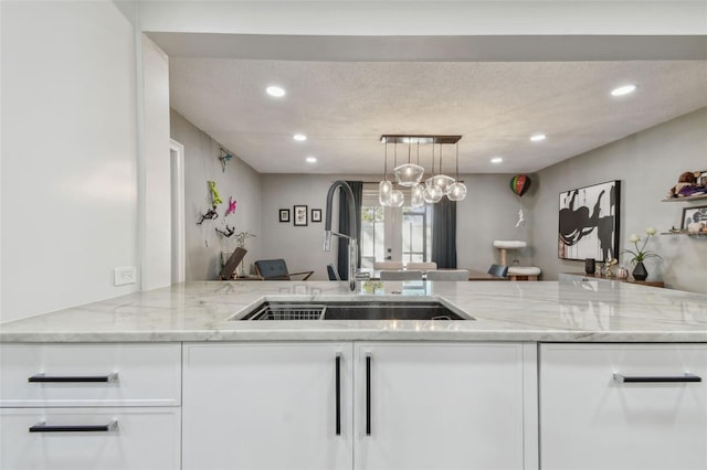 kitchen featuring french doors, sink, light stone countertops, decorative light fixtures, and white cabinetry