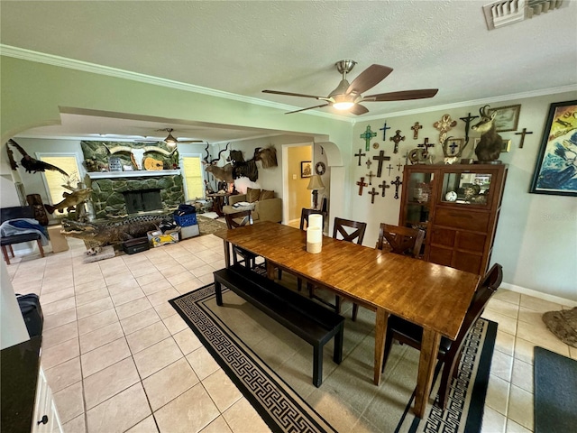 tiled dining area featuring a textured ceiling, a fireplace, ceiling fan, and crown molding