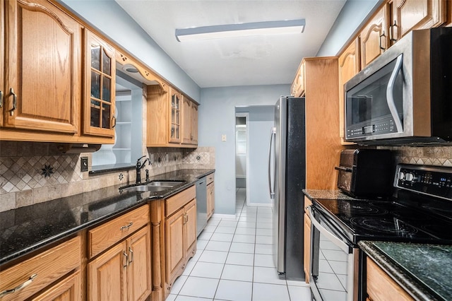 kitchen with sink, dark stone countertops, light tile patterned floors, appliances with stainless steel finishes, and tasteful backsplash