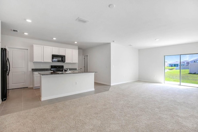 kitchen featuring dark stone counters, black appliances, white cabinets, an island with sink, and light colored carpet