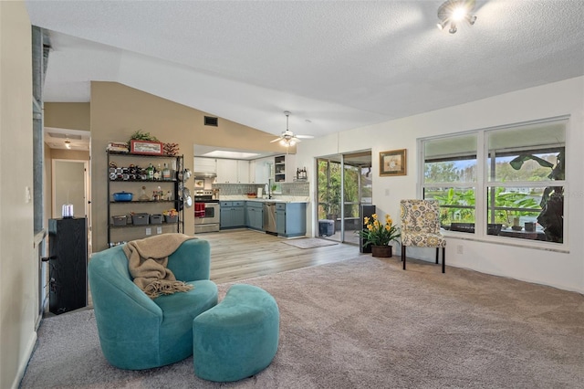 living room with light carpet, a textured ceiling, vaulted ceiling, ceiling fan, and sink