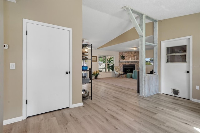 entrance foyer featuring a textured ceiling, a stone fireplace, light hardwood / wood-style flooring, and lofted ceiling