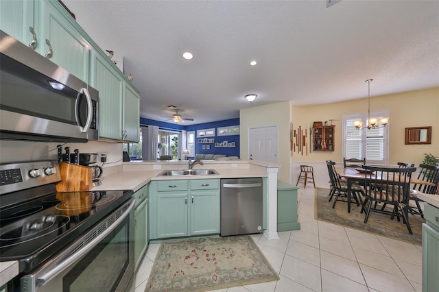 kitchen featuring ceiling fan with notable chandelier, stainless steel appliances, sink, light tile patterned floors, and pendant lighting