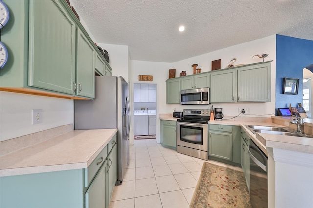 kitchen with washer and clothes dryer, sink, green cabinetry, a textured ceiling, and stainless steel appliances