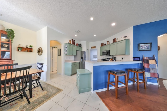 kitchen with kitchen peninsula, appliances with stainless steel finishes, light tile patterned floors, and green cabinets