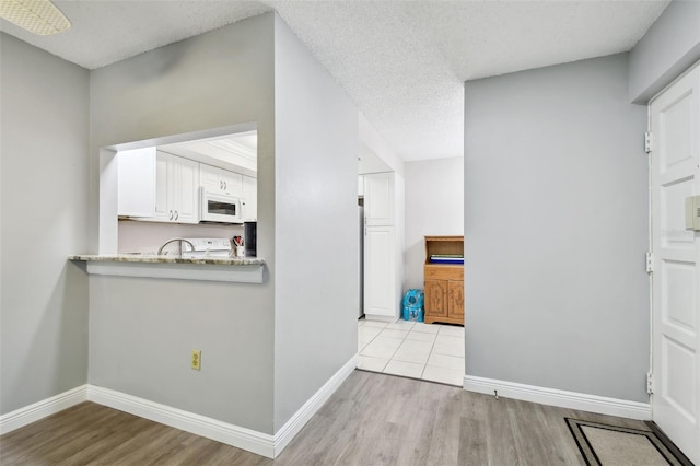 kitchen with light stone counters, white cabinets, light hardwood / wood-style floors, and a textured ceiling