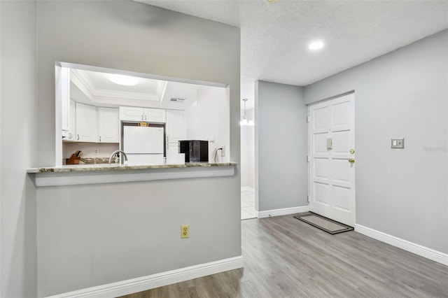 kitchen featuring white cabinets, white refrigerator, a raised ceiling, crown molding, and light hardwood / wood-style flooring