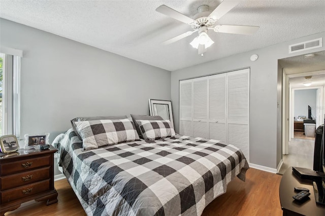 bedroom with ceiling fan, dark hardwood / wood-style floors, a textured ceiling, and a closet