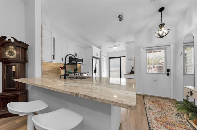 kitchen featuring white cabinetry, kitchen peninsula, stainless steel fridge, pendant lighting, and a breakfast bar area