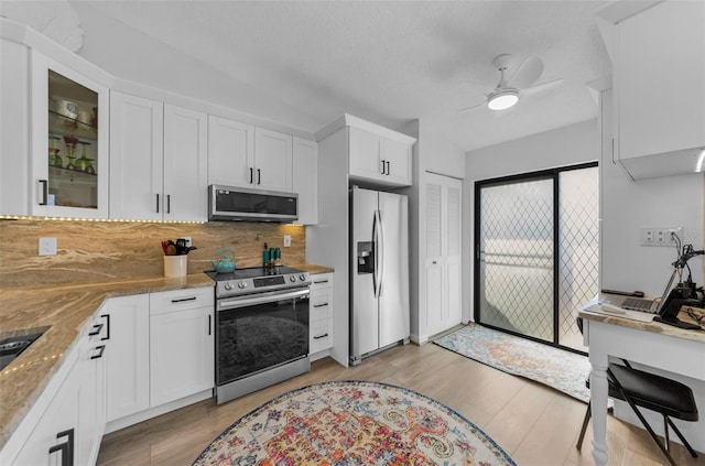 kitchen with light stone counters, stainless steel appliances, ceiling fan, white cabinets, and light hardwood / wood-style floors