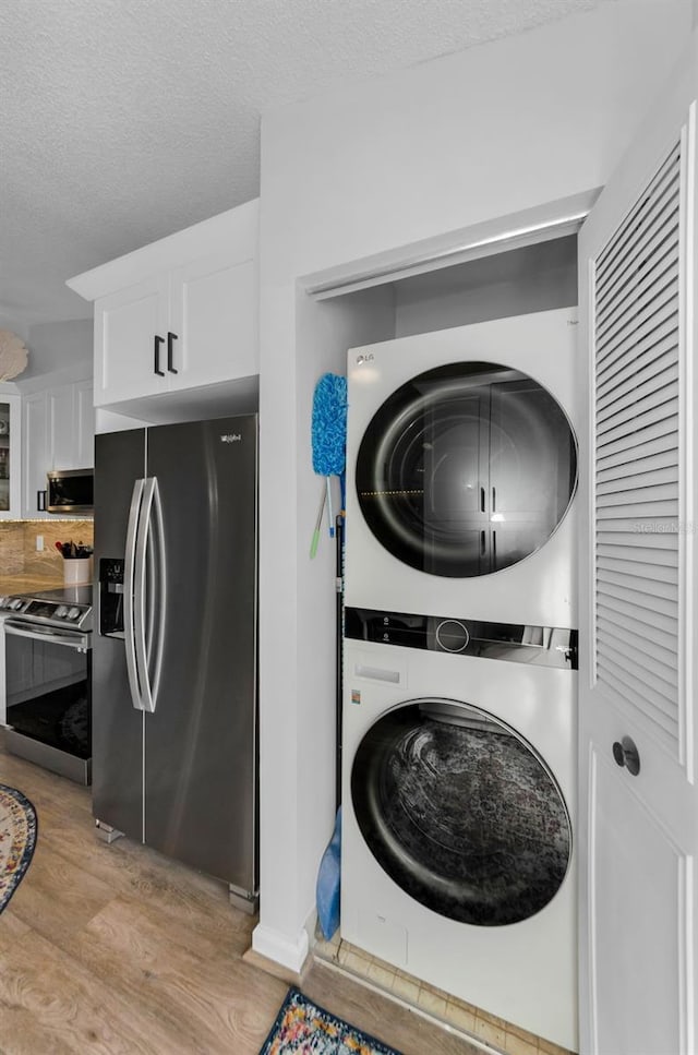 washroom featuring a textured ceiling, light wood-type flooring, and stacked washer / dryer