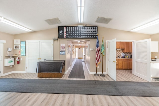 interior space with a textured ceiling, tasteful backsplash, light hardwood / wood-style floors, and vaulted ceiling