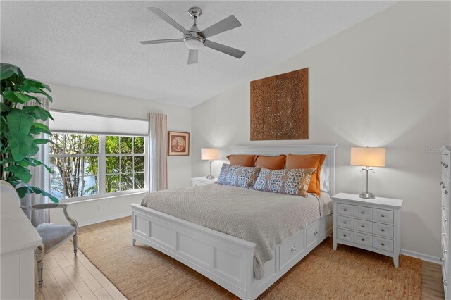 bedroom featuring ceiling fan, lofted ceiling, a textured ceiling, and light wood-type flooring