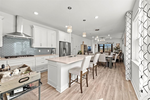 kitchen with wall chimney exhaust hood, decorative light fixtures, white cabinetry, stainless steel appliances, and decorative backsplash