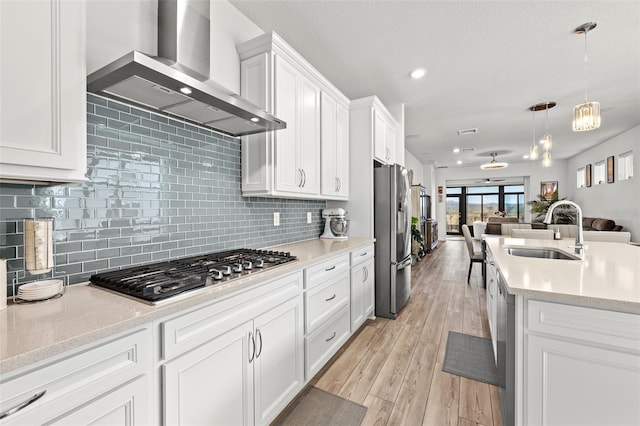 kitchen with wall chimney range hood, pendant lighting, sink, white cabinetry, and stainless steel appliances