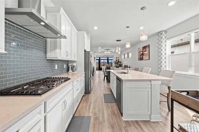 kitchen featuring sink, hanging light fixtures, appliances with stainless steel finishes, white cabinets, and wall chimney exhaust hood