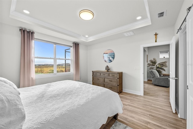 bedroom featuring crown molding, a barn door, light wood-type flooring, and a tray ceiling