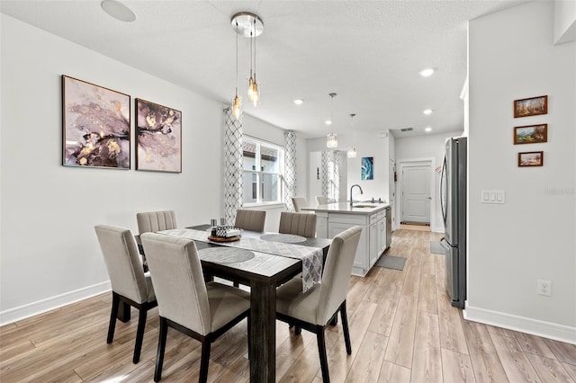 dining room featuring sink, a textured ceiling, and light wood-type flooring