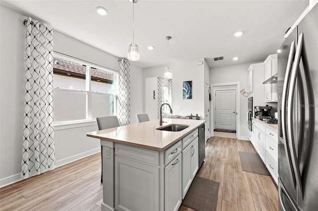 kitchen featuring white cabinetry, a center island with sink, stainless steel appliances, pendant lighting, and sink