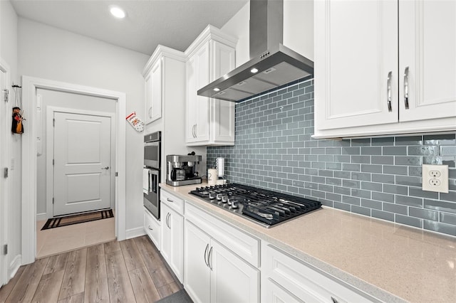 kitchen featuring range hood, light hardwood / wood-style floors, decorative backsplash, white cabinetry, and stainless steel appliances