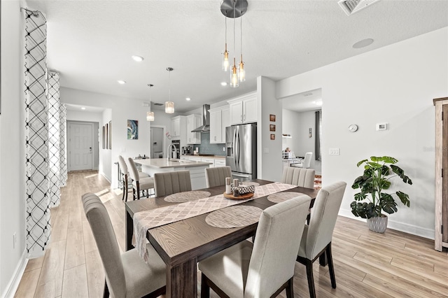 dining space featuring a textured ceiling, a chandelier, light hardwood / wood-style flooring, and sink