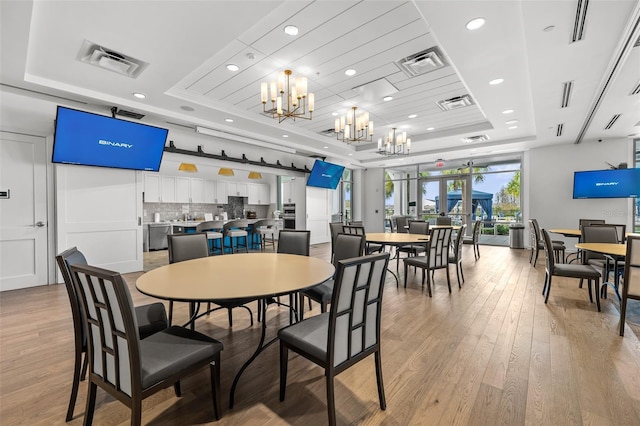 dining space with light hardwood / wood-style floors, french doors, a raised ceiling, and a chandelier