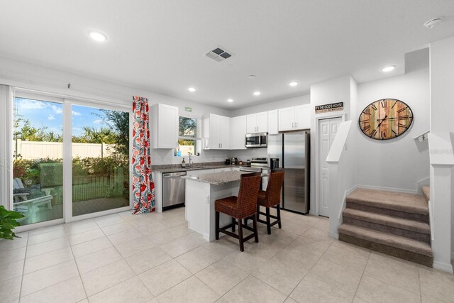 kitchen featuring light stone countertops, a center island, a breakfast bar area, white cabinets, and appliances with stainless steel finishes