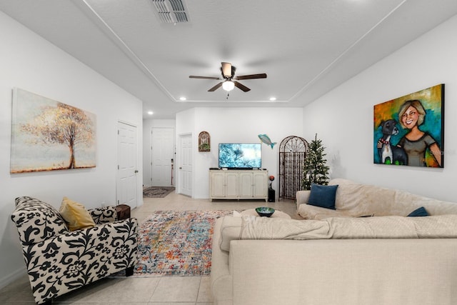 living room featuring a raised ceiling, ceiling fan, and light tile patterned floors