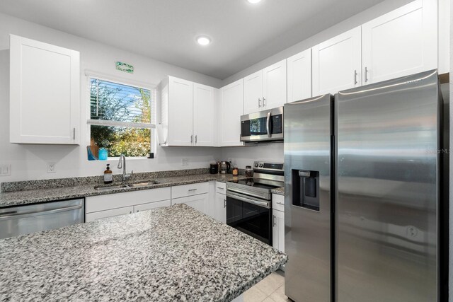 kitchen with white cabinetry, sink, stainless steel appliances, light stone counters, and light tile patterned flooring