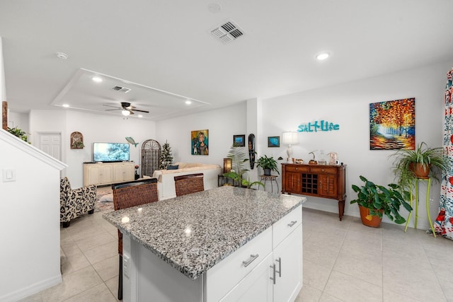 kitchen featuring white cabinetry, a center island, ceiling fan, light stone countertops, and light tile patterned floors