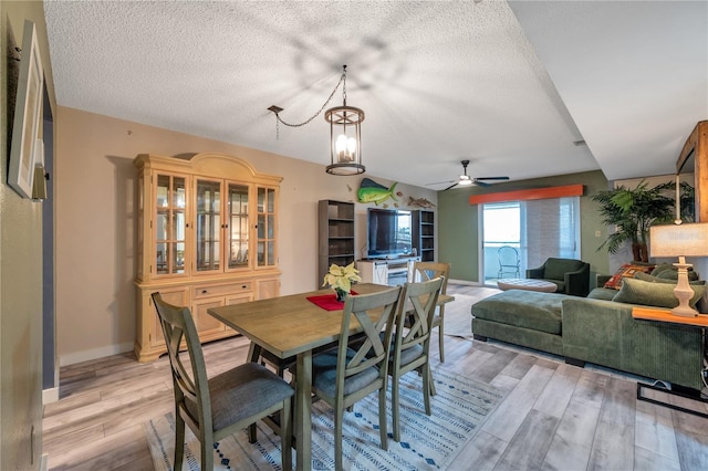 dining space with ceiling fan with notable chandelier, a textured ceiling, and light hardwood / wood-style flooring