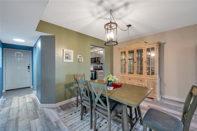 dining room with light hardwood / wood-style floors, a textured ceiling, and an inviting chandelier