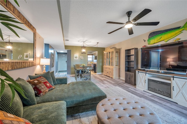 living room featuring ceiling fan, a textured ceiling, and light wood-type flooring