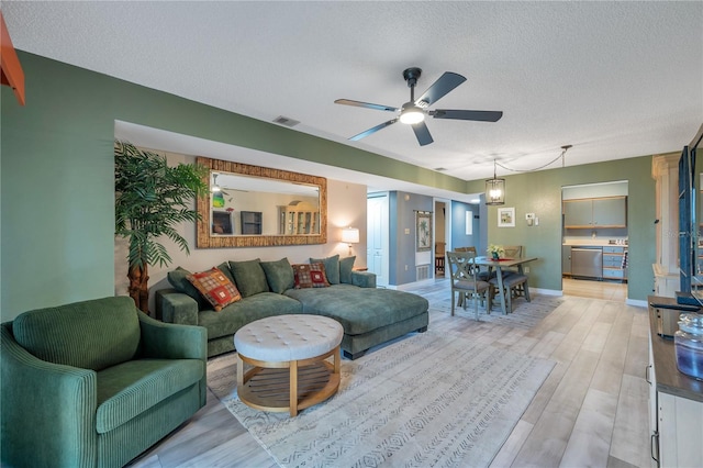 living room with ceiling fan, a textured ceiling, and light wood-type flooring