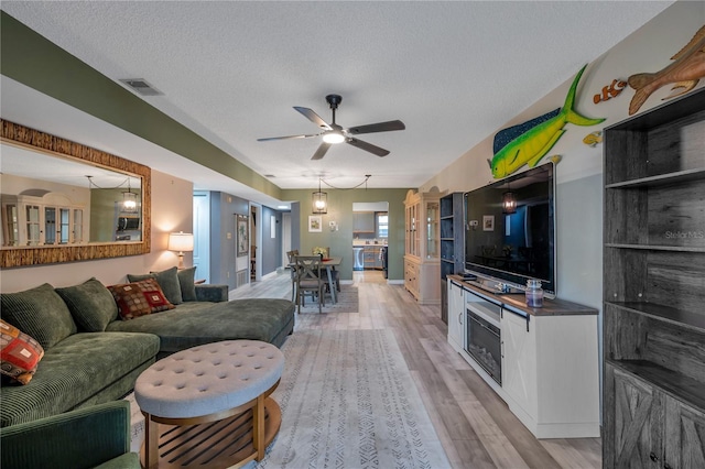 living room featuring ceiling fan, light hardwood / wood-style floors, and a textured ceiling