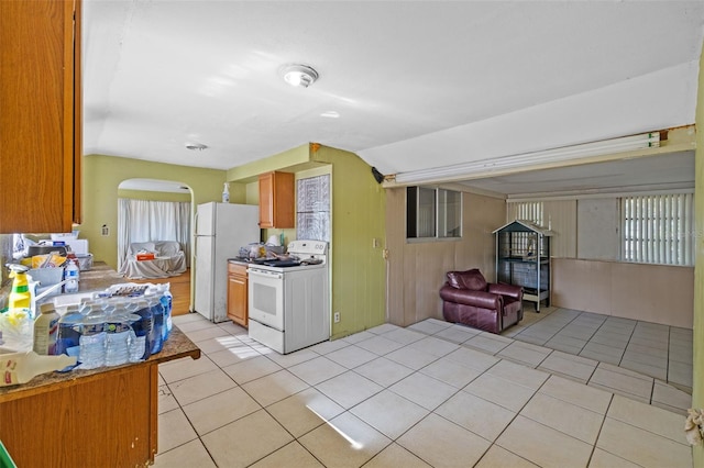 kitchen featuring wood walls, lofted ceiling, light tile patterned flooring, and white appliances