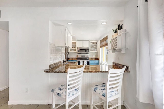 kitchen featuring kitchen peninsula, appliances with stainless steel finishes, sink, light tile patterned floors, and white cabinets