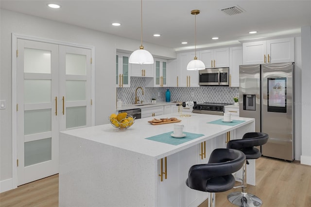 kitchen with sink, hanging light fixtures, stainless steel appliances, white cabinets, and a kitchen island