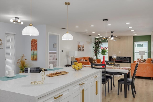 kitchen featuring white cabinetry, light hardwood / wood-style flooring, a kitchen island, pendant lighting, and ceiling fan