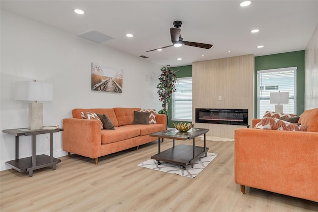 living room featuring ceiling fan, a large fireplace, and light hardwood / wood-style floors