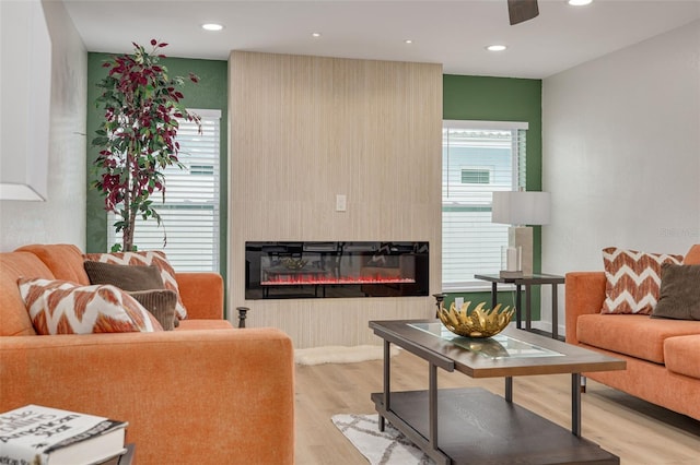 living room with ceiling fan, a large fireplace, plenty of natural light, and light wood-type flooring