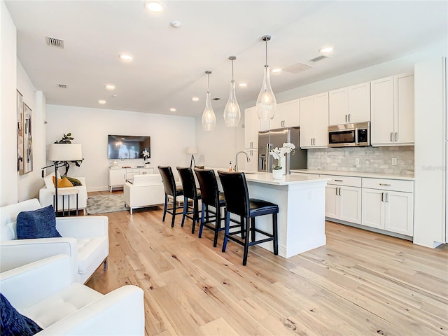 kitchen featuring backsplash, a breakfast bar, stainless steel appliances, decorative light fixtures, and a center island with sink