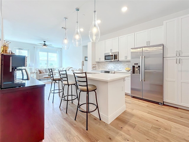 kitchen featuring decorative backsplash, stainless steel appliances, pendant lighting, white cabinets, and a center island