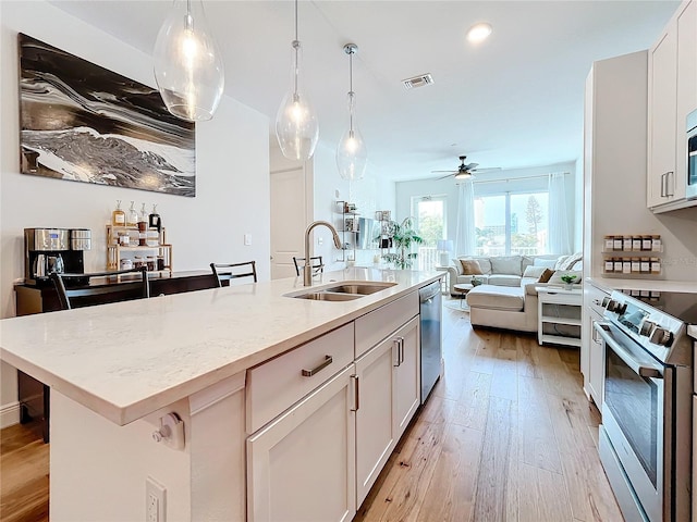 kitchen with sink, stainless steel appliances, light stone counters, a kitchen island with sink, and white cabinets