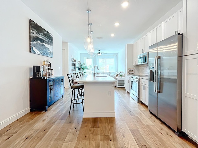 kitchen featuring light wood-style flooring, stainless steel appliances, a sink, white cabinets, and a kitchen bar