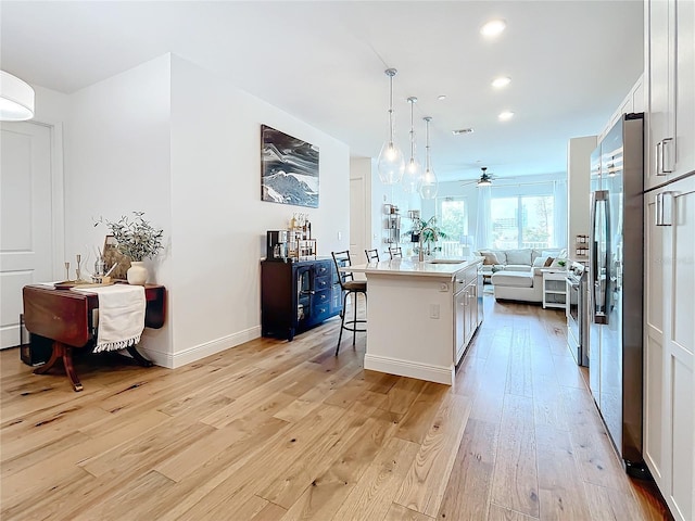 kitchen featuring a breakfast bar area, light wood finished floors, light countertops, open floor plan, and white cabinets