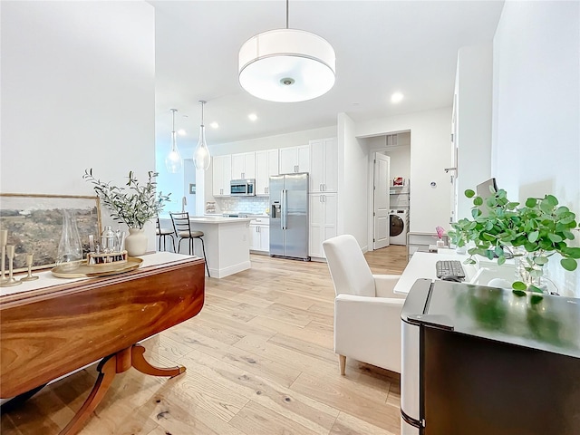 interior space featuring tasteful backsplash, appliances with stainless steel finishes, light wood-style floors, white cabinetry, and washer / dryer