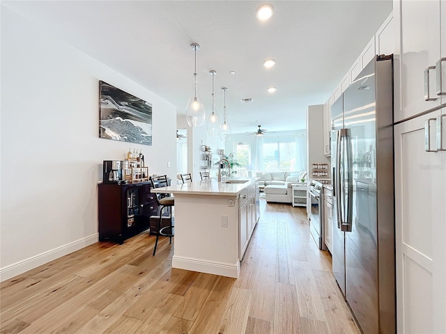 kitchen featuring light wood-style flooring, appliances with stainless steel finishes, open floor plan, white cabinetry, and a sink